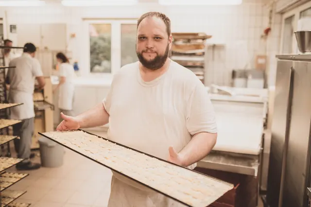 Bäcker präsentiert ein Backblech mit frischem Gebäck in der Backstube Rorup