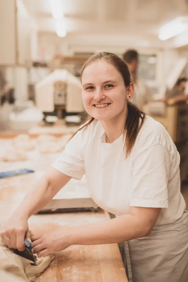 Bäckerin lächelt bei der Teigarbeit in der Backstube