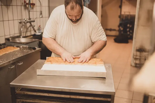 Bäcker schneidet frisch gebackenen Blechkuchen