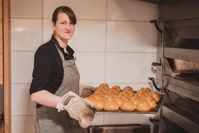 Mitarbeiterin holt frische Brötchen aus dem Ofen im Verkaufsraum