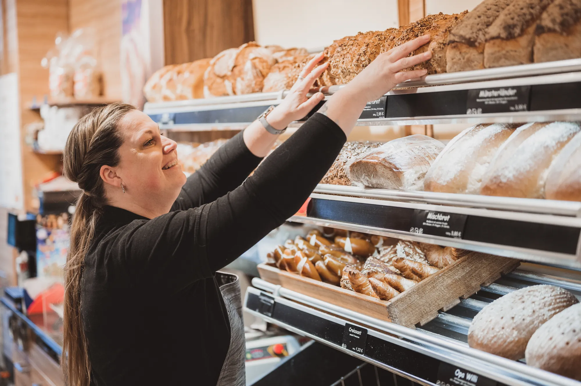 Verkäuferin greift ein Brot aus dem Brotregal