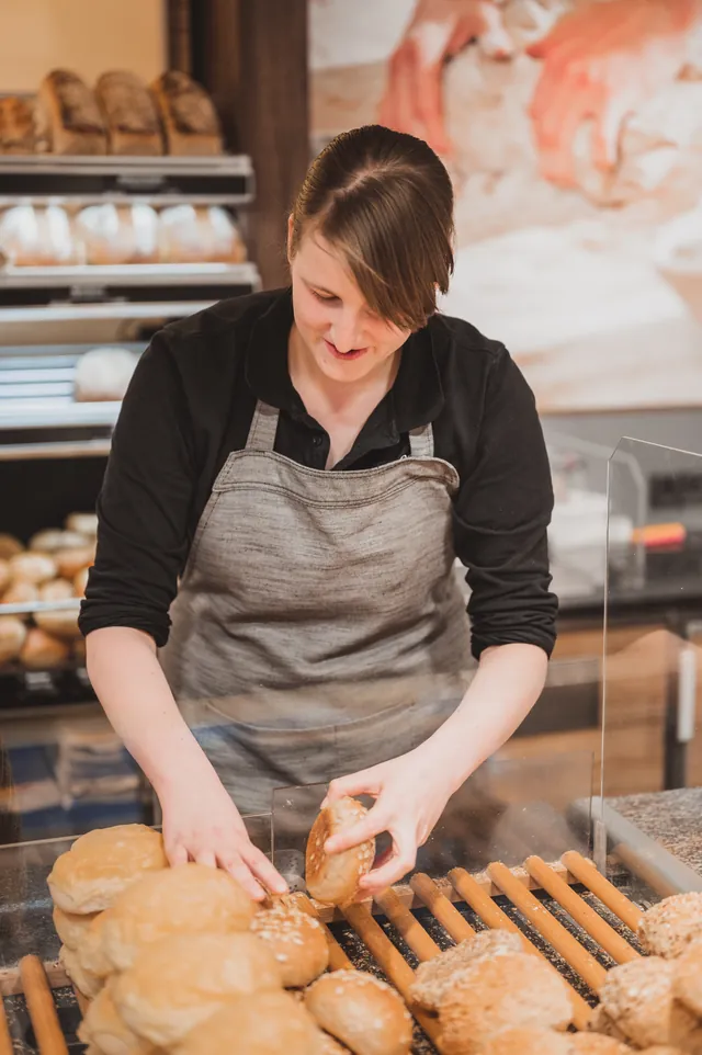 Verkäuferin legt Brötchen in die Verkaufstheke