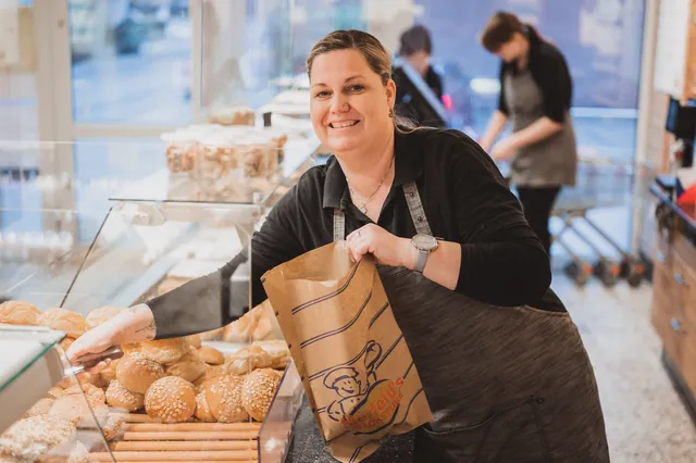 Verkäuferin packt Brötchen in eine Papiertüte an der Theke